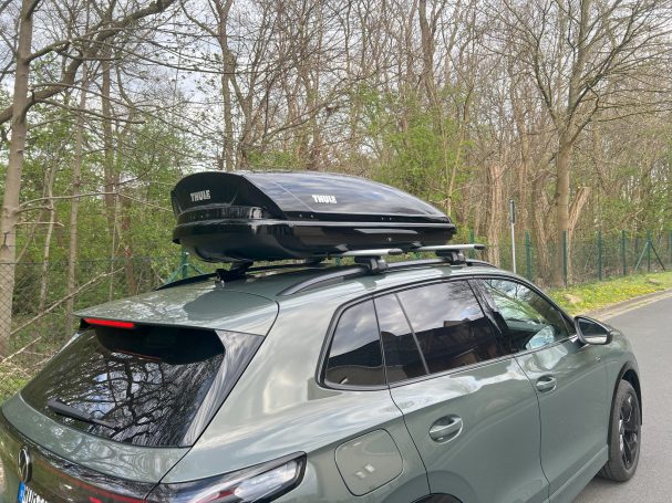 Dachträger mit schwarzem Gepäckträger auf einem Wagen, umgeben von Bäumen.