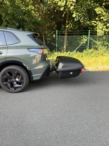 Ein SUV mit einem angehängten schwarzen Anhänger auf einem Straßenstück.
