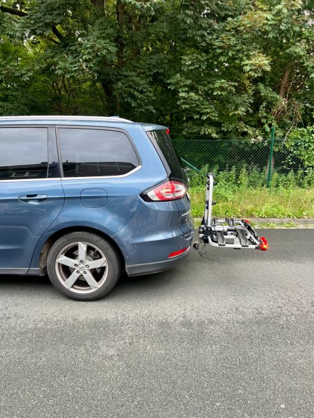 Blauer Wagen mit Montage für Fahrräder am Heck, geparkt an einer Straße.