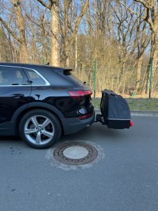 Schwarzes SUV mit Gepäckträger auf der Rückseite, in der Nähe eines Baumes.