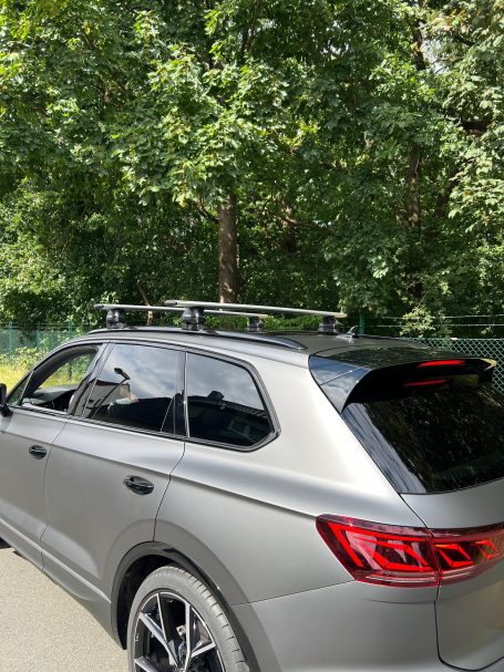 Silberner SUV mit Dachgepäckträger, parkend in einer grünen Umgebung.