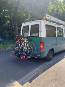 Ein blau-grüner Lieferwagen mit zwei Fahrrädern auf dem Heckträger.