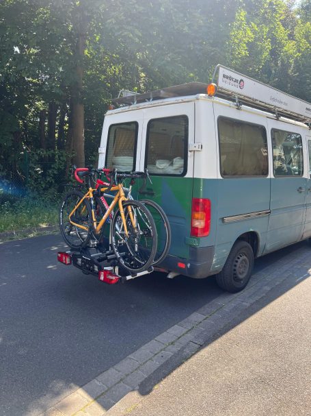 Blauer Lieferwagen mit zwei Fahrrädern auf einem Trägersystem hinten.