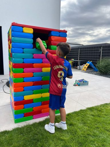 Ein Kind in Fußballtrikot baut mit bunten Bauklötzen. Klares Wetter im Hintergrund.