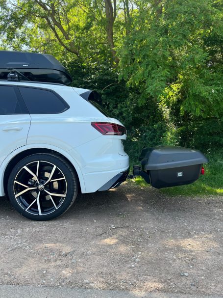 Weiße SUV mit Fahrradträger, parkend in einer grünen Umgebung.