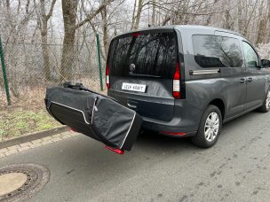 Ein dunkler Van mit einer schwarzen Gepäckträger-Tasche hinten.