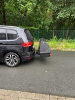 Schwarzer SUV mit montierter Fahrradträger am Heck, parkend auf einer Straße.
