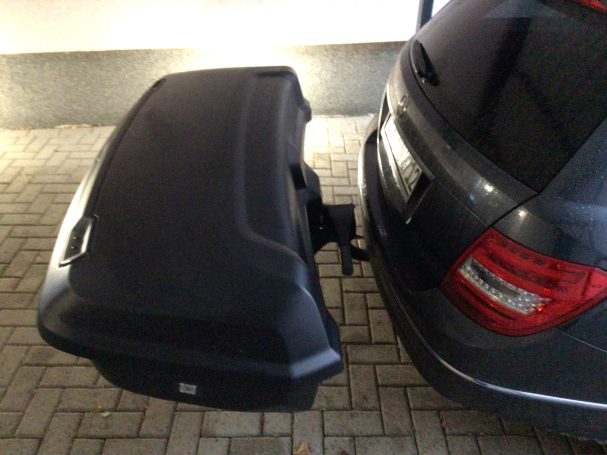 Schwarzer Gepäckträger am Heck eines Fahrzeugs, befestigt an der Anhängerkupplung.