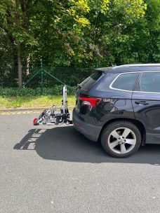 Fahrradträger am Heck eines schwarzen SUVs auf einem Parkplatz mit Bäumen im Hintergrund.