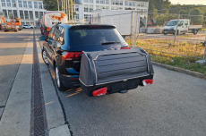 Schwarzes Auto mit einer abgedeckten Ladefläche, parkt auf einem asphaltierten Platz.