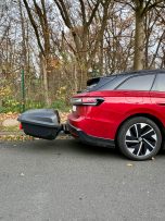 Roter SUV mit schwarzem Anhänger, geparkt in einer Waldumgebung.