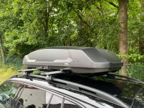 Dachbox auf einem Auto, montiert auf einem Dachträger, vor grünem Hintergrund.