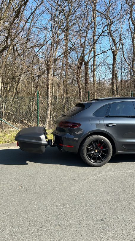 Schwarzer SUV mit angehängtem Gepäckträger auf einem Weg durch einen Wald.