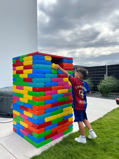 Ein Junge baut mit bunten Steckbausteinen einen hohen Turm im Garten.